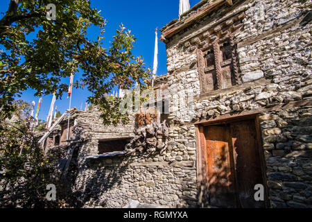 Facciate delle case del borgo nella parte superiore della valle Marsyangdi e colorati di preghiera buddista bandiere svolazzanti Foto Stock