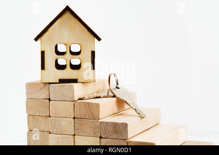 Toy casa in legno su scale di legno con chiavi, realty concetto con sfondo luminoso Foto Stock