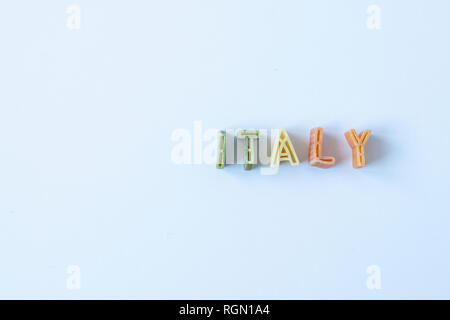 La parola "l'Italia" composta con pasta reale lettere in bandiera italiana di colori su una superficie bianca. Sfondo con copia spazio sulla sinistra. Foto Stock