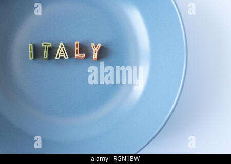 La parola "l'Italia" composta con pasta reale lettere in bandiera italiana i colori in un piatto blu. Sfondo con copia spazio sulla destra. Foto Stock