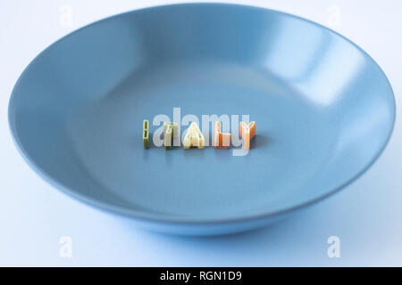 La parola "l'Italia" composta con pasta reale lettere in bandiera italiana i colori in un piatto blu. Vista laterale. Foto Stock