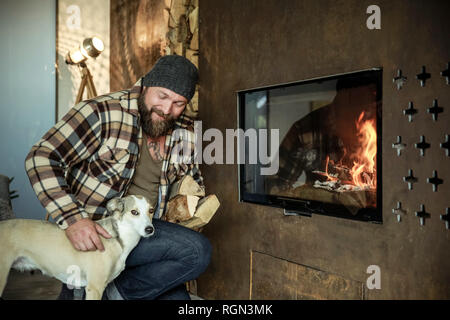 Uomo Barbuto con il suo cane di fronte al caminetto a casa Foto Stock