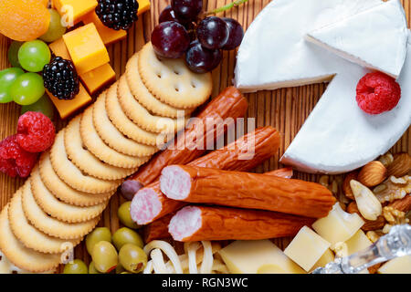 Vista dettagliata dei vari tipi di gourmet le fette di formaggio con stampo green olive nere e verdi e noci sul piatto di legno su sfondo sfocato Foto Stock