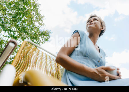 Basso angolo di visione della donna seduta in giardino con tazza di caffè Foto Stock