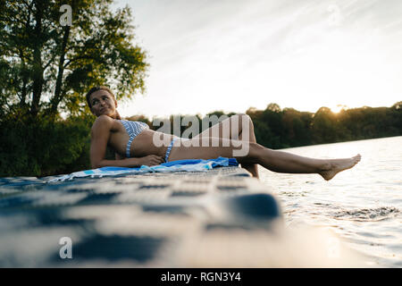 Donna che indossa un bikini giacente su un galleggiante in un lago Foto Stock