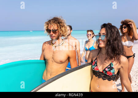Amici divertendosi, passeggiate sulla spiaggia, portando le tavole da surf Foto Stock
