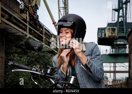 Sorridente giovane donna mettendo sul casco del motociclo Foto Stock