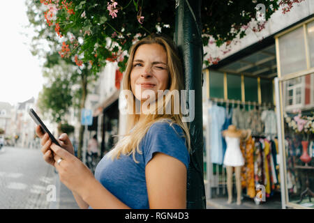 Paesi Bassi, Maastricht, sorridente ragazza con un telefono cellulare nella città scintillanti Foto Stock