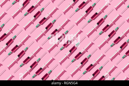 Siringhe multipli organizzati in un pattern su sfondo rosa Foto Stock