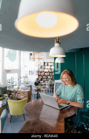 Sorridente giovane donna utilizzando laptop in un cafe Foto Stock