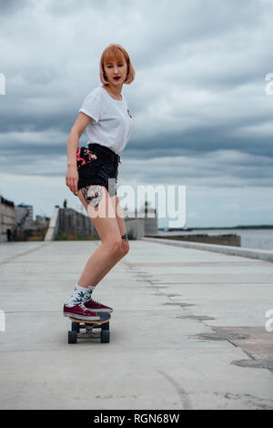 Giovane donna cavallo carver skateboard al Riverside Foto Stock