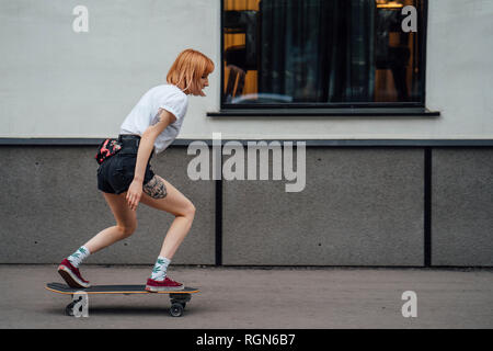 Giovane donna cavallo carver skateboard sul marciapiede Foto Stock