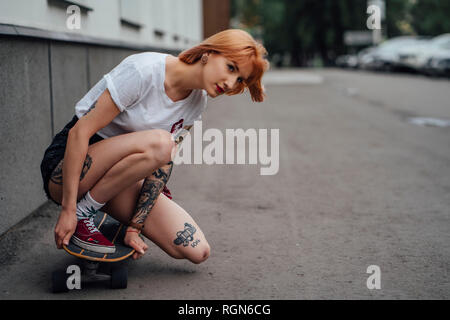 Giovane donna accovacciata sul carver skateboard su una strada Foto Stock