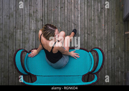 Giovane donna seduta sul lettino turchese sulla terrazza, vista dall'alto Foto Stock