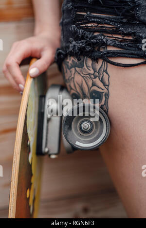 Close-up di tatuati giovane donna appoggiata su skateboard Foto Stock