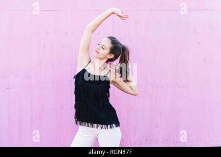 Sorridente giovane donna stiramento nella parte anteriore della parete di rosa Foto Stock