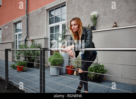 Fiducioso giovane donna indossando giacca biker appoggiata sulla ringhiera di balcone Foto Stock