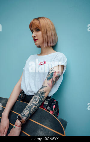 Cool giovane donna holding carver skateboard in piedi alla parete turchese Foto Stock