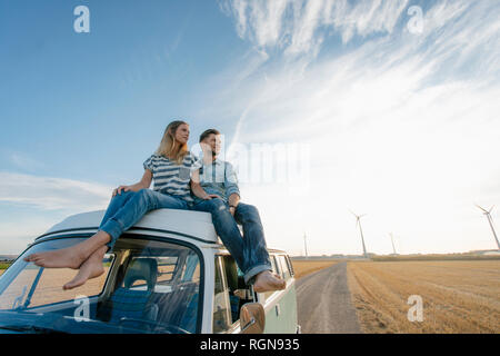 Giovane seduto sul camper van nel paesaggio rurale con le turbine eoliche in background Foto Stock