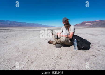 Stati Uniti, California, Valle della Morte, uomo seduto a terra nel deserto con map avente un periodo di riposo Foto Stock