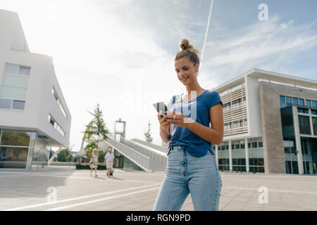 Paesi Bassi, Maastricht, sorridente giovane donna utilizzando il cellulare in città Foto Stock