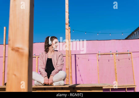 Rilassata giovane donna seduta sulla piattaforma di ascolto di musica Foto Stock