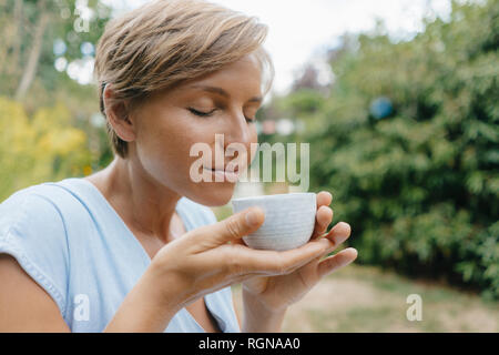 Ritratto di donna con gli occhi chiusi in giardino azienda tazza di caffè Foto Stock
