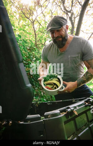 Uomo maturo scartando scarti di cucina sul palo di composto Foto Stock