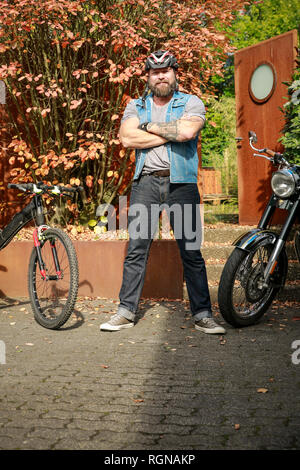 Ritratto di uomo in piedi tra moto e bicicletta Foto Stock