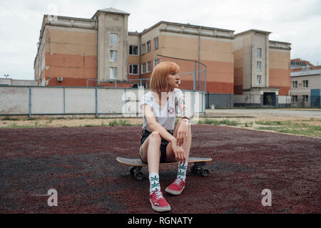 Giovane donna seduta su carver skateboard all'aperto Foto Stock