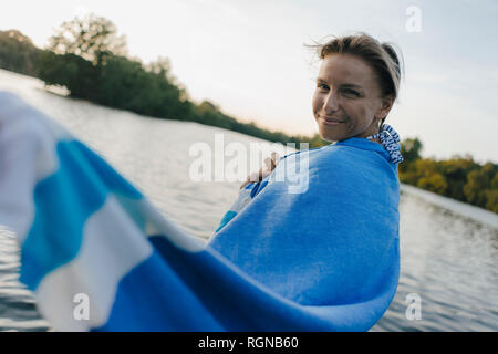 Ritratto di donna sorridente avvolto in un asciugamano in un lago Foto Stock