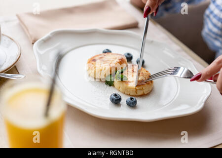 Bella giovane donna tagli pancake con un coltello. Una leggera colazione con caffè vicino alla finestra in una caffetteria. Foto Stock