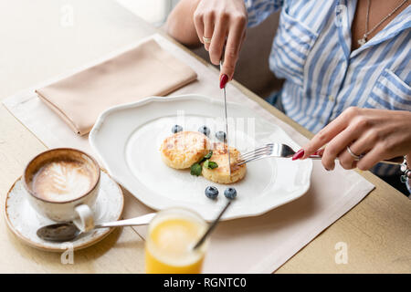 Bella giovane donna tagli pancake con un coltello. Una leggera colazione con caffè vicino alla finestra in una caffetteria. Foto Stock