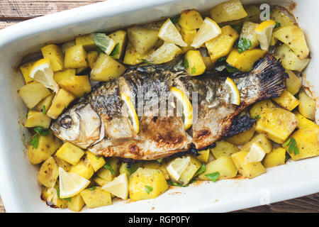 Pesce al forno carpa con le patate in una pentola di ceramica. Stile rustico Foto Stock