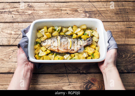 Pesce al forno carpa con le patate in una pentola di ceramica. Stile rustico Foto Stock