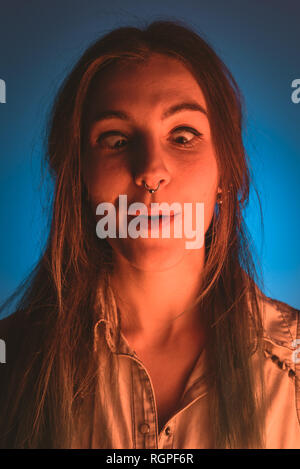 Ragazza con piercing facendo facce buffe in arrossamento su sfondo blu Foto Stock