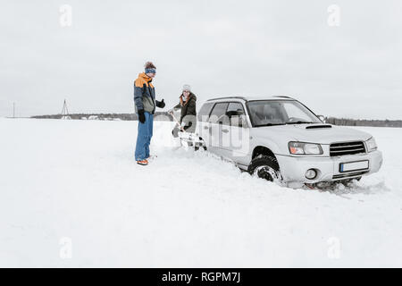 Signora giovane con la pala di scavo da neve automobile nei pressi di guy in inverno indossare sul prato in Vilnius, Lituania Foto Stock
