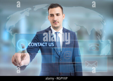 Uomo di toccare contattaci tasto utilizzando il dito indice sul display trasparente con il telefono e la posta elettronica e i simboli sulla mappa del mondo sullo sfondo Foto Stock