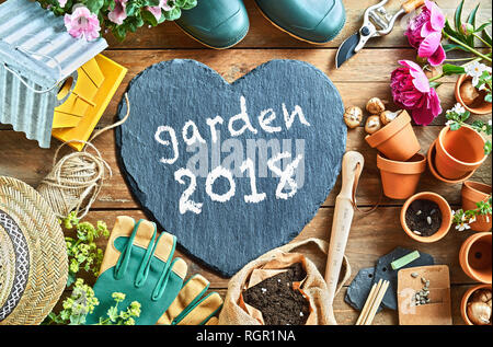 Giardino stagione 2018 concetto foto aeree di attrezzature da giardinaggio disposti sul pavimento, con il grigio a forma di cuore con la scheda di iscrizione in bianco Foto Stock