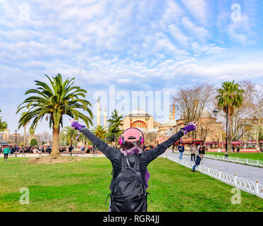 Bella donna nel cappuccio con cuffie solleva due bracci abbracciando Sultanahmet Park a Istanbul, Turchia.concetto di libertà , libertà sensazione sfondo Foto Stock