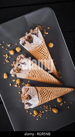 Tre congelate coni gelato guarnita con cioccolato e servita con dadi di fresco su un elegante rettangolare piatto nero visto dal di sopra Foto Stock