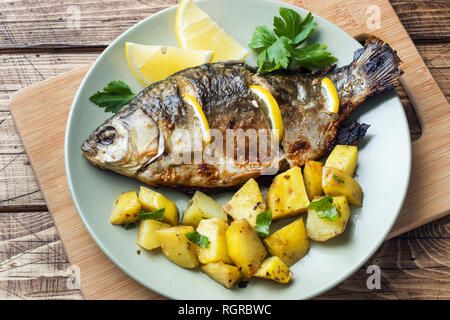 Pesce al forno carpa con il limone verde e patate su una piastra. Sfondo di legno Foto Stock