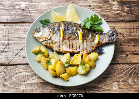 Pesce al forno carpa con il limone verde e patate su una piastra. Sfondo di legno Foto Stock