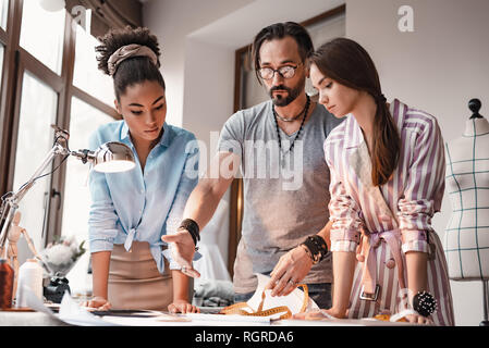 Il chief designer mostra la nuova idea. Vista inferiore di giovani designer sono il disegno e pensando di nuovo vestito. Foto Stock