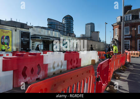 Rosso e bianco barriere di opere di fronte alla stazione ferroviaria di Woking town, Surrey, Regno Unito Foto Stock