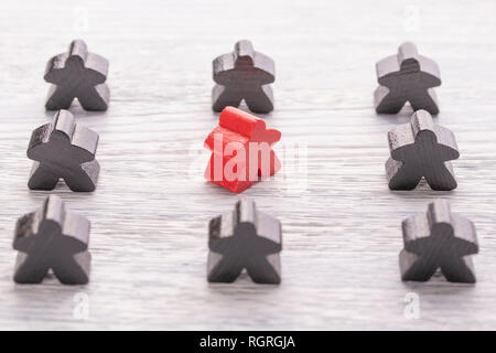 Unicità e individualità e differenza. In legno rosso figura in una folla di diverso colore su una bianca tavolo in legno. Il concetto di disaccordo con th Foto Stock