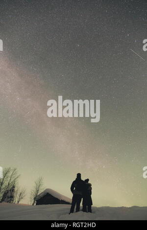 Vista posteriore di giovane e donna che si abbracciano e ammirano il bel cielo notturno nella campagna artica Foto Stock
