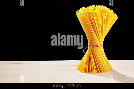 Golden spaghetti legati in un mazzetto di stringa colorati su un rustico tavolo in legno con uno sfondo nero e copia di spazio. Foto Stock