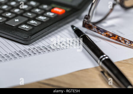 Calcolatrice ,occhiali e penna giacciono sul documento finanziario sul tavolo di legno. In primo piano Foto Stock