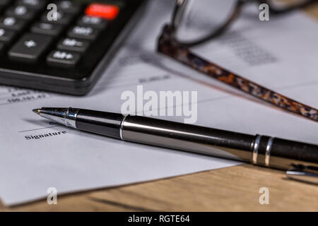 Forniture per ufficio - Calcolatrice, occhiali, penna e documento giacciono sul tavolo di legno Foto Stock